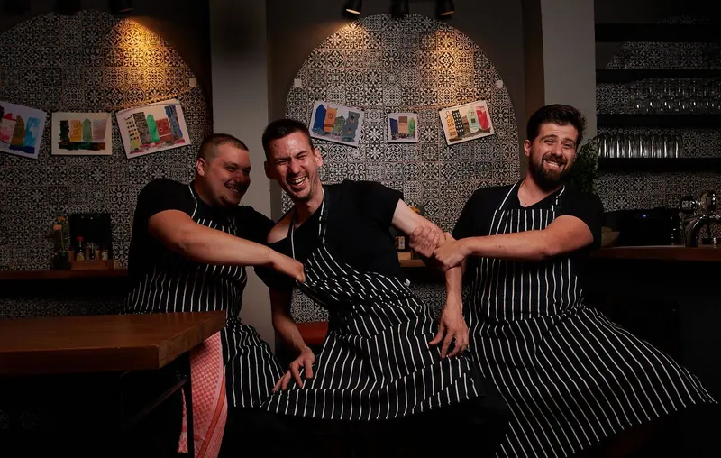 Three KAI chefs in striped aprons laughing in the dining room